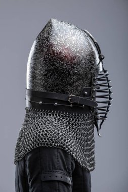 Ribbed Faceplaka ve Zincirli Kask. Bu görüntü koyu, muhtemelen karartılmış bir çeliği, sivri uçlu bir miğferi ve yatay kaburgaları olan belirgin bir yüz plakasını gösteriyor. Kaskın tabanından bir zincirli tasma uzanıyor..
