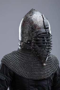 Ribbed Faceplaka ve Zincirli Kask. Bu görüntü koyu, muhtemelen karartılmış bir çeliği, sivri uçlu bir miğferi ve yatay kaburgaları olan belirgin bir yüz plakasını gösteriyor. Kaskın tabanından bir zincirli tasma uzanıyor..