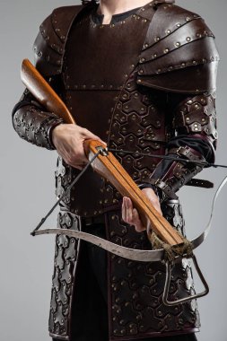 Deri Zırhlı Savaşçı elinde yaylı tüfek tutuyor. Bu resim, üzerinde çivili detaylar olan kahverengi deri bir zırh bulunan bir kişinin elinde metal bir çubukla ahşap bir yaylı tüfek tuttuğunu gösteriyor..