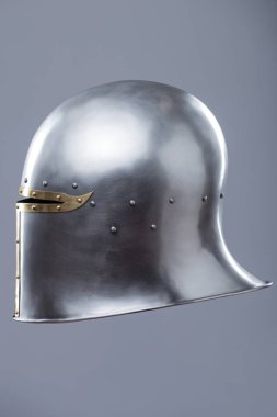 Brass Trim 'li Gümüş Ortaçağ Barbute Miğferi. Bu resim parlak gümüş bir miğfer gösteriyor. Yüzünde belirgin bir T-şekli var. Pirinç süsleme ve perçinlerle vurgulanıyor..