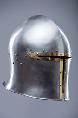 Brass Trim 'li Gümüş Ortaçağ Barbute Miğferi. Bu resim parlak gümüş bir miğfer gösteriyor. Yüzünde belirgin bir T-şekli var. Pirinç süsleme ve perçinlerle vurgulanıyor..