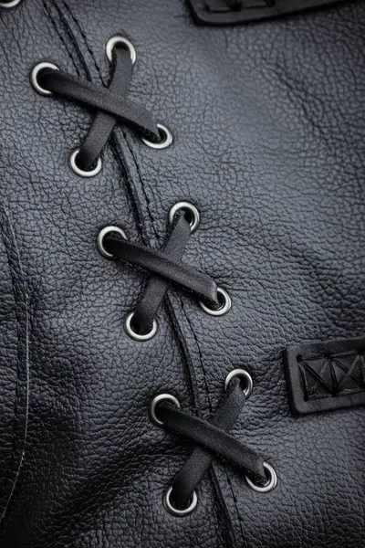 Siyah Deri Ceket Bağlama 'nın yakın çekimi. Bu resim siyah deri kolsuz ceketin yanındaki dekoratif bağlama detaylarının yakın çekimini gösteriyor. Siyah bağcıklar gümüş göz bebeklerinden geçirilir ve çapraz çapraz desen oluşturur..