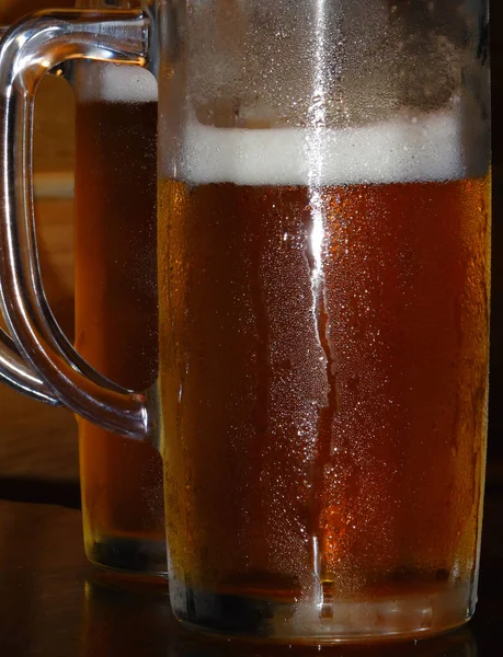 Two tall beer glasses with massive handles are filled with chilled beer