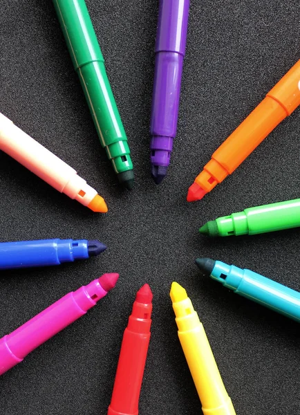 Open felt-tip pens of different colors in the shape of a star lie on a black background vertical photo