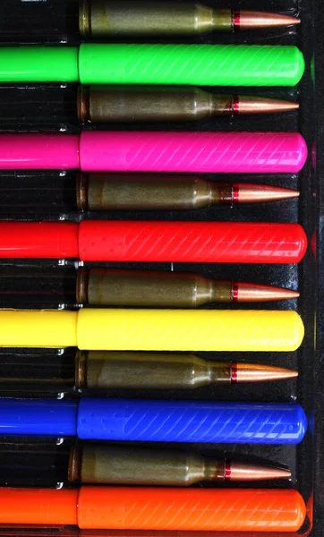 Caps Of Colored Felt Tip Pens And Rifle Bullets Laid Out Together In A Pen Case. Concept Photo To Illustrate Art And War