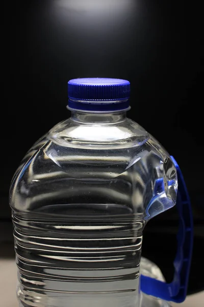A large bottle with a plastic handle filled with clean water over black background