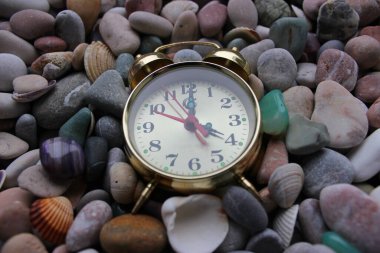 Old copper alarm clock on smooth colored pebbles and seashells