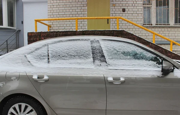 A car parked near a residential building with frozen windows and door handles covered with snow