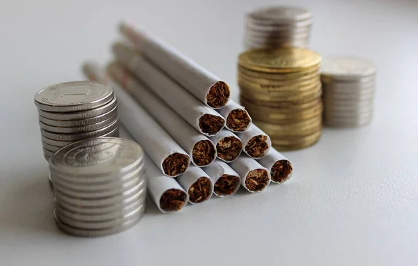 Filter cigarettes and blurred coins in a columns on a white surface isolated stock photo
