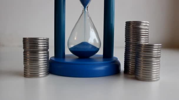 時間概念ストックビデオの価格の象徴として近くの時間ガラスとコインで砂のトリクルを流れる — ストック動画