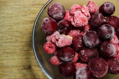 Tahta yüzeyde cam bir kasede çözünmüş bir sürü kırmızı böğürtlen.