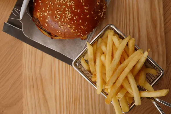 Tahta bir tahtanın üzerindeki metal bir sepetin içinde büyük bir hamburger ve kızarmış patates. 