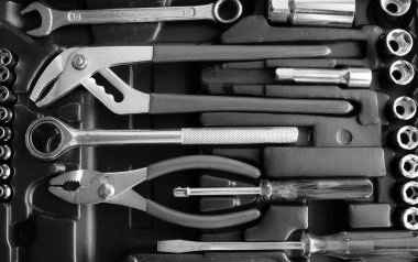 Çelik anahtarlar, pense, mandallı soketler ve tornavidalar plastik alet çantasının üst görünümünde.