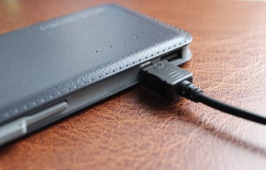 Siyah USB kablosu, deri döşeme yakın açılı boşaltılan bir güç bankasına bağlı.