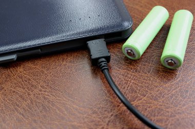 Kahverengi deri yüzeyde zarif deri güç bankasının yanında iki AA batarya. 
