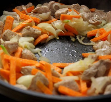 Kızarmış et ve doğranmış soğan ve havuçla birlikte tavadan buhar yükselir.