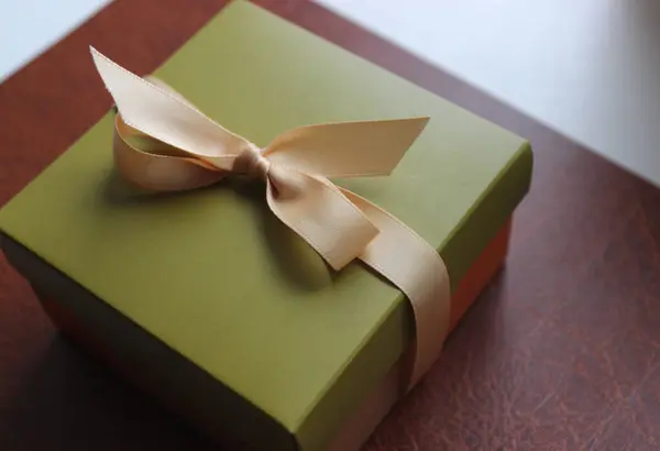 Business gift wrapping in olive tones with an elegant beige ribbon on brown leather