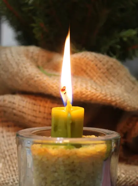 Fire Of Dark Yellow Wax Candle In Glass Candlestick Filled With Grains Near Handmade Burlap Wrapping