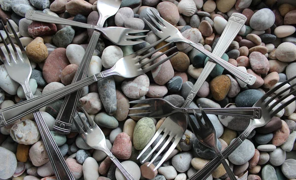 Identical Silvery Dessert Forks Laid Out In A Row On Colored Sea Stones