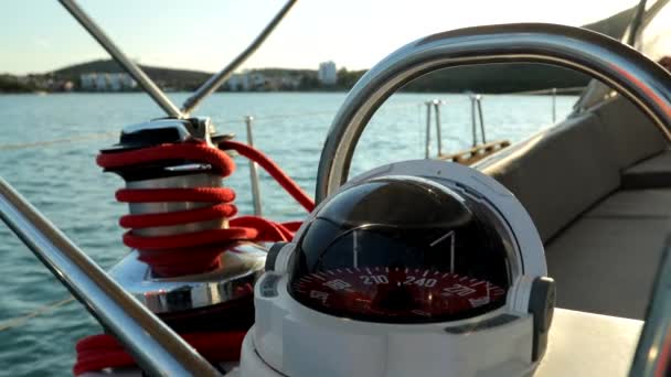 ボード上の球状ヨットコンパスの回転 ロッキー海岸近くを回るセイルボート — ストック動画