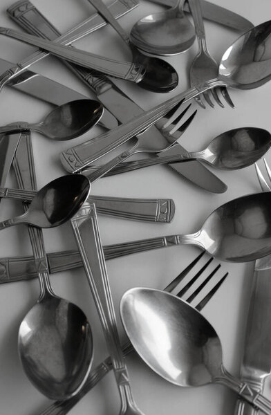 Used stainless steel forks, spoons and knives scattered on white surface vertical stock photo