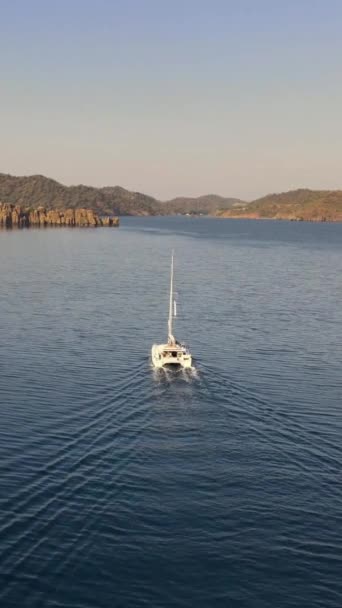 解压后的航行船卡塔马兰游艇漂流至落基海岸附近的悬崖岛垂直故事的鱼群视频 — 图库视频影像