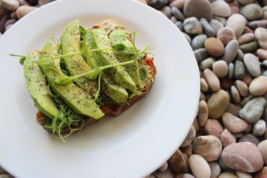 Mikroçim ve baharatlar bir tostun üzerinde, sebzeler temiz beyaz tabağın üzerinde renkli çakıl taşlarının üzerinde. 
