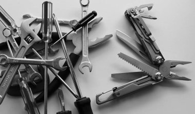Monochrome image of blades and screws of steel multi-tool VS pile of hand tools dumped in disarray
