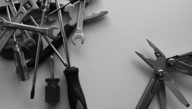 Grayscale image of opened multi tool and a stack of variety tools on white workbench