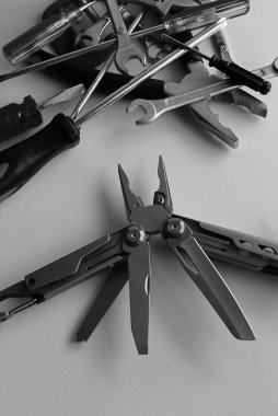 Folding utility multi-tool with opened blades against a bunch of unnecessary tools monochrome stock image
