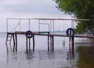 Nehrin diğer tarafında eski lastikleri ve nükleer santrali olan eski bir iskelenin korkulukları.