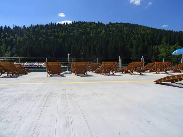 stock image Elegant wooden sun loungers on the fenced embankment of a forest lake