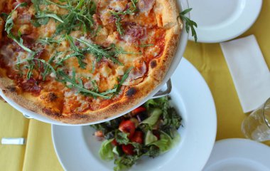 Restoran masası seti. Masa başında pizza servisi ve taze sebze salatası. 