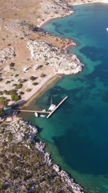 Küçük bir marinası olan güzel bir deniz koyunun dikey videosu ve masmavi deniz manzaralı demirli yatlar.