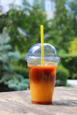 Tahta masadaki soğuk turuncu espresso ile doldurulmuş plastik bardağın yan görüntüsü. 
