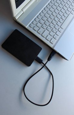 Gri ölçekli dizüstü bilgisayara eklenmiş USB kablosu olan siyah taşınabilir HDD