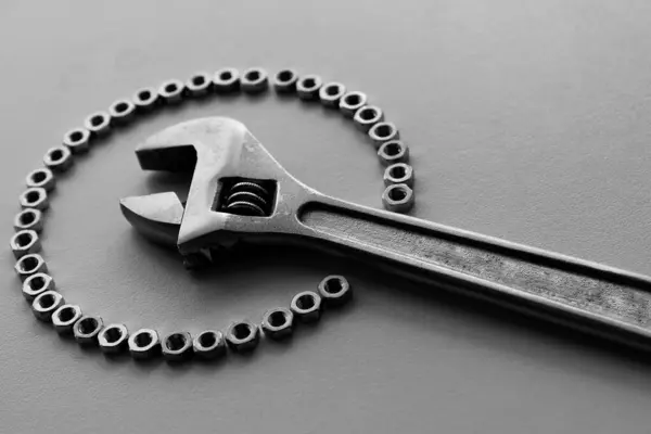 stock image Head of adjustable wrench inside of perfect circle made with fastener nuts grayscale stock image. Mechanical workshop illustrative background 