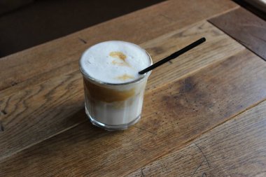 Köpük kapaklı buzlu kahve ve siyah ahşap masadaki cam tüple kaplanmış. 