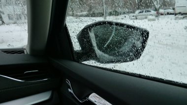Kış sabahı şehir otoparkında. Araba tarafındaki pencere ve aynaya ıslak kar ve soğuk damlalar. 