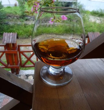 Elit Kehribar Konyağı ile dolu olan Üçüncü Cam Yakından Bakış. Özel Konağın Terasındaki Ahşap Masada Klasik Konyak Camı