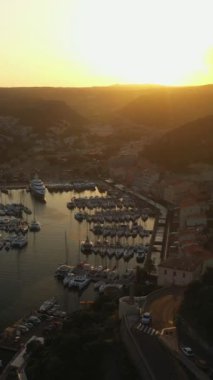Yat limanının etrafında eski evler olan antik bir kasabada günbatımının dikey videosu. Gün batımında demirli yatları ve yelkenli hava görüntüleriyle şehir limanında.  