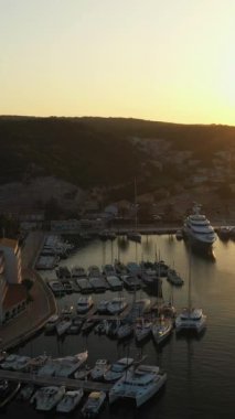 Şehir rıhtımlarının hava görüntüleri. Yelkenli yatları, güneş doğarken, koruma altındaki kayalık bir körfeze demirlemiş. Deniz kıyısında bir yat marinası ve deniz kenarında son güneş ışınlarının dikey videosu.