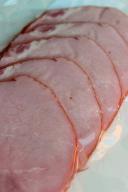 İnce dilimlenmiş jambon parçacıkları vakum paketinde beyaz masa yakın görüntüsünde.