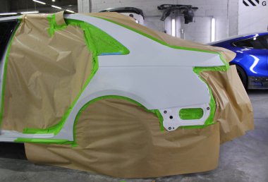 Araba gövdesi panellerinin son boya katmanlarını ve koruyucu vernikleri uygulamak için hazır yüzeyleri. Beyaz bir arabanın arka çamurluğu kaportacıda boyamaya hazırlanıyor.