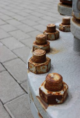 Yeraltı yakıt tankının yuvarlak metal kapağında bir sıra kıvrılmış paslı fındık. 