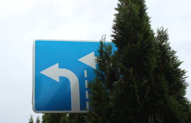 Otomobil Yolu 'nun kenarındaki Uzun Ağaçlar İki şeritten Sola Dönmeye İzin Veren Mavi Uyarı İşareti