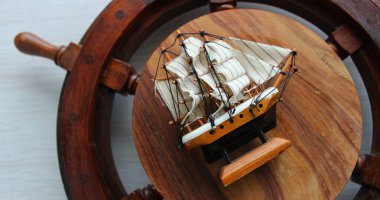 Düz bir şekilde, eski bir geminin tekerleğinin üzerinde bir yelkenli gemi figürünün ayrıntılı görüntüsü duruyordu.