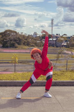 Joven afro de cabello naranja bailando al estilo urbano en parque local pista de atletismo, vejetaryen y cielo hermosos de fondo