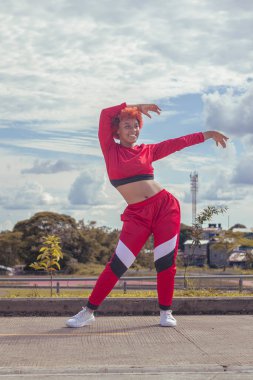 Joven afro de cabello naranja bailando al estilo urbano en parque local pista de atletismo, vejetaryen y cielo hermosos de fondo