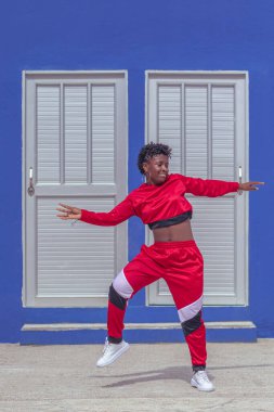 Jover mujer afro realiza baile estilo urban on parque local con save azul y puertas de fondo